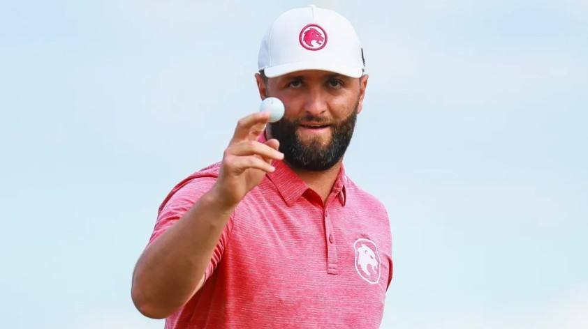 Jon Rahm holding up his golf ball on the green